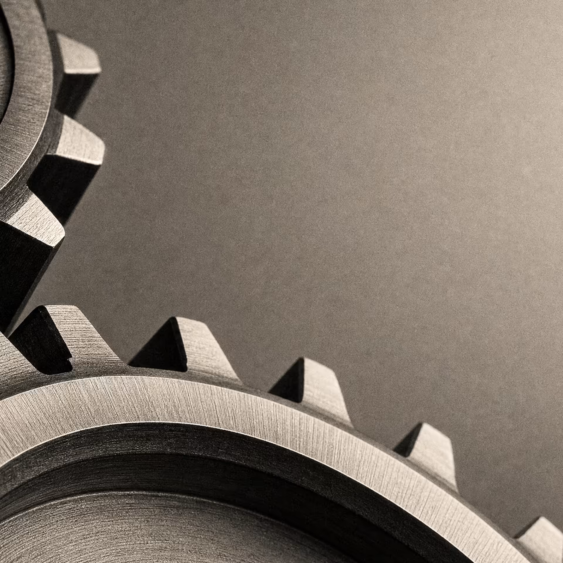 Two interlocking steel gears meshing at their teeth, lit hard from one side in black and white, the machined edges sharp against deep shadow.