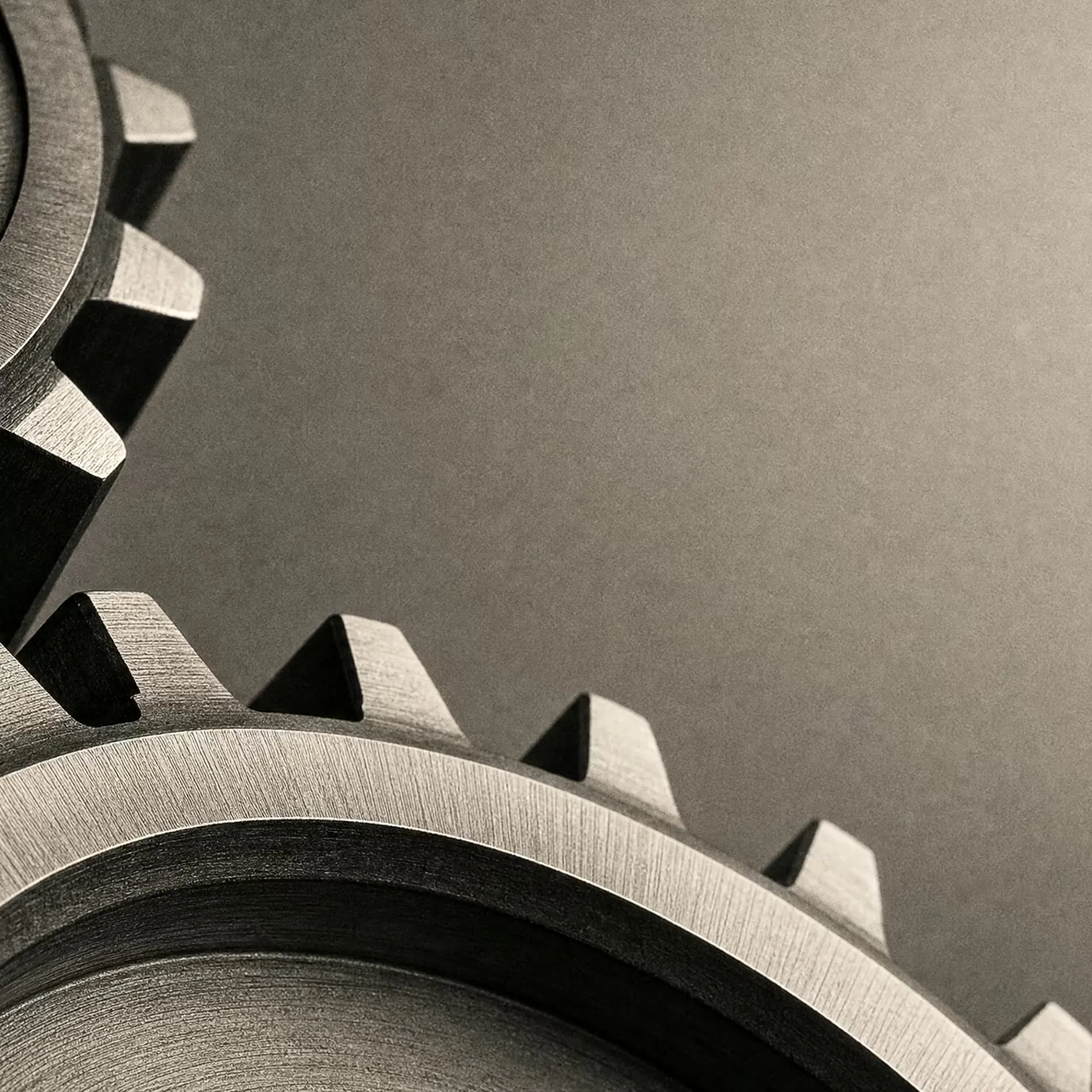 Two interlocking steel gears meshing at their teeth, lit hard from one side in black and white, the machined edges sharp against deep shadow.