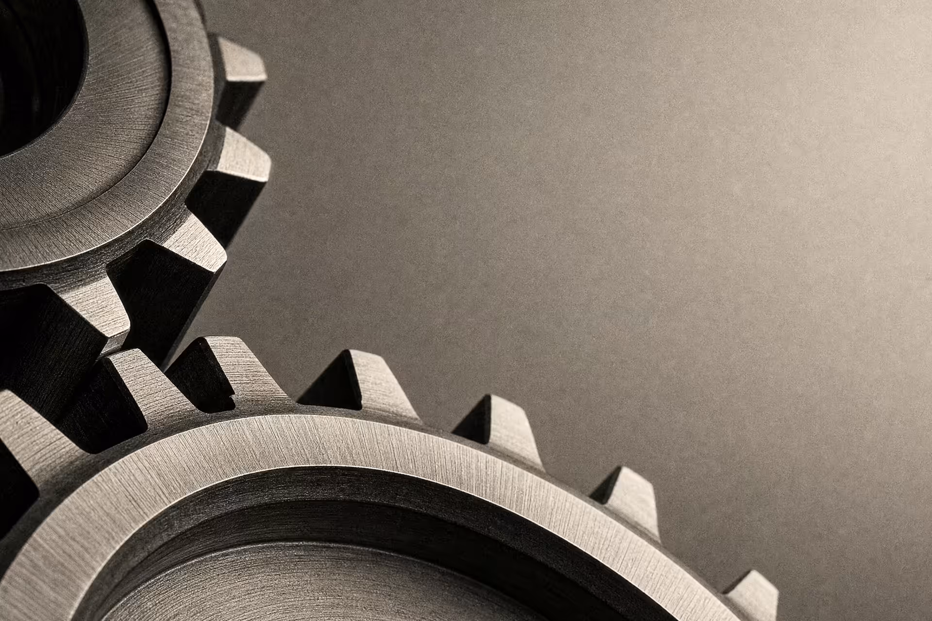 Interlocking machined-steel gears meshing at close range in warm-tone monochrome, tooling marks raking across the teeth under a single side light.