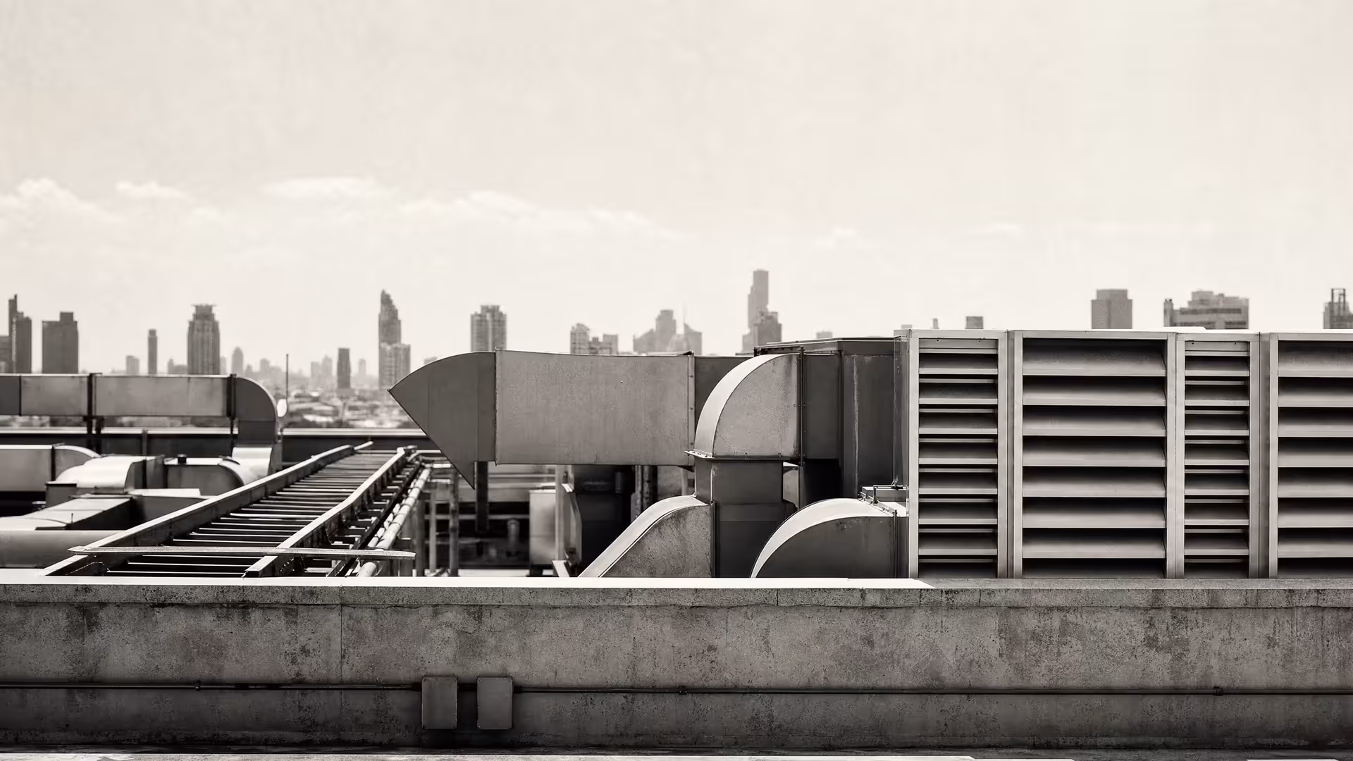 Bangkok office-building rooftop in warm-tone monochrome: HVAC ducts and metal louvres in sharp geometry, hazy city silhouettes reduced to tonal bands above.