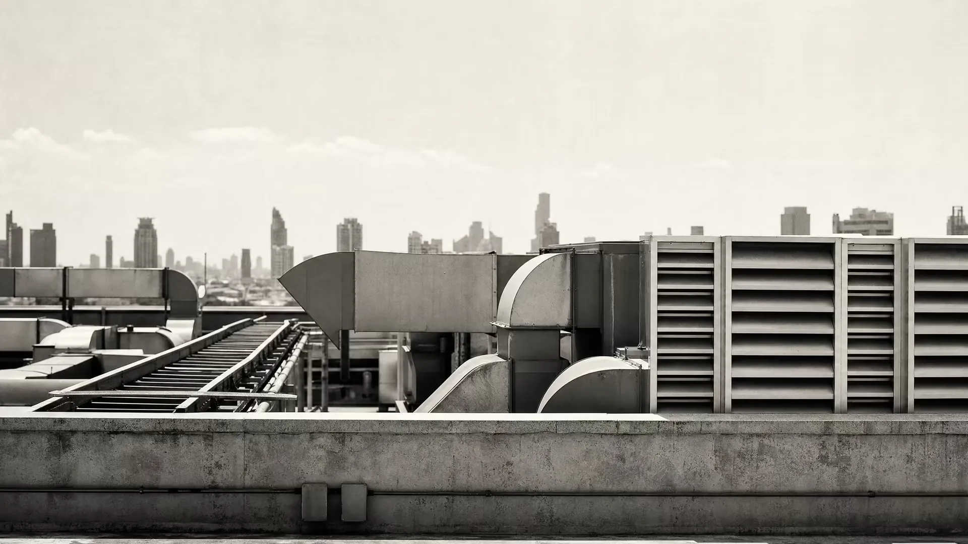 Bangkok office-building rooftop in warm-tone monochrome: HVAC ducts and metal louvres in sharp geometry, hazy city silhouettes reduced to tonal bands above.