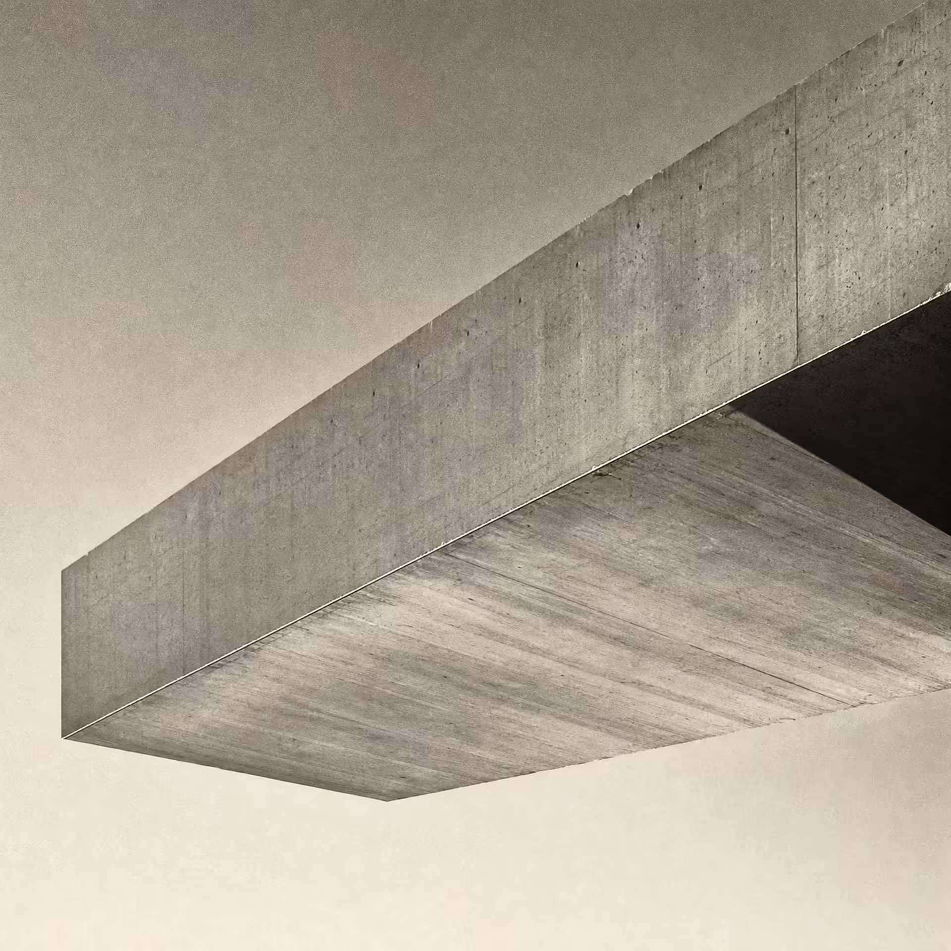 A concrete cantilever beam projecting over open space from a single anchored support in warm-tone monochrome, the lit soffit reaching across an empty sky under grazing daylight.