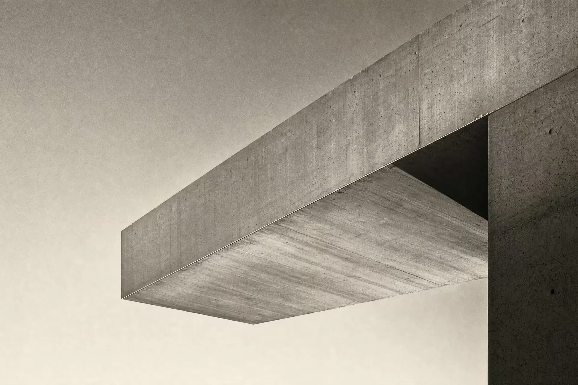 A concrete cantilever beam projecting over open space from a single anchored support in warm-tone monochrome, the lit soffit reaching across an empty sky under grazing daylight.