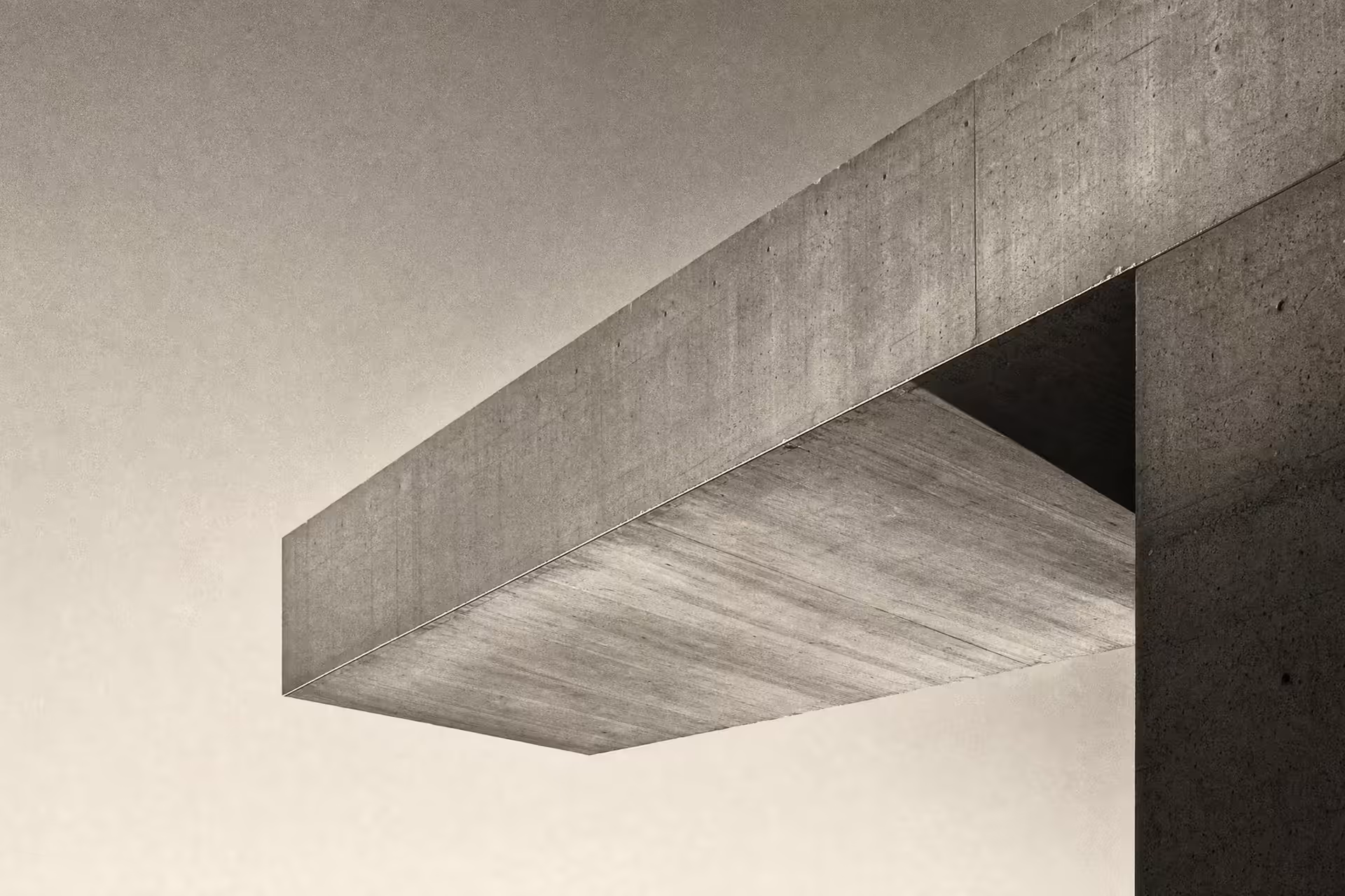 A concrete cantilever beam projecting over open space from a single anchored support in warm-tone monochrome, the lit soffit reaching across an empty sky under grazing daylight.