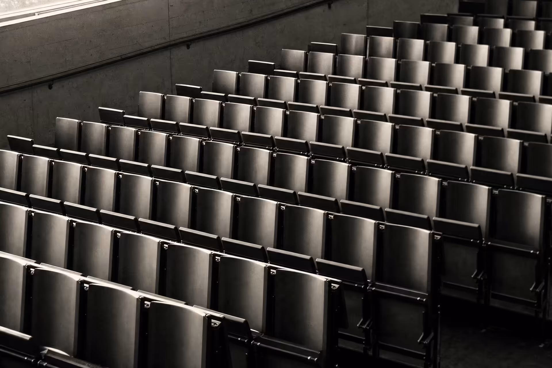An empty tiered lecture hall, repeating rows of seats receding across the frame, warm-tone monochrome.