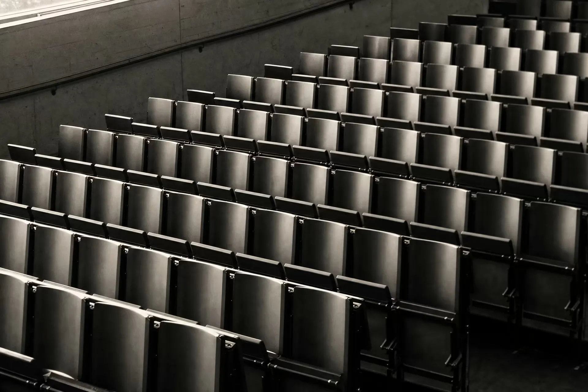 An empty tiered lecture hall, repeating rows of seats receding across the frame, warm-tone monochrome.