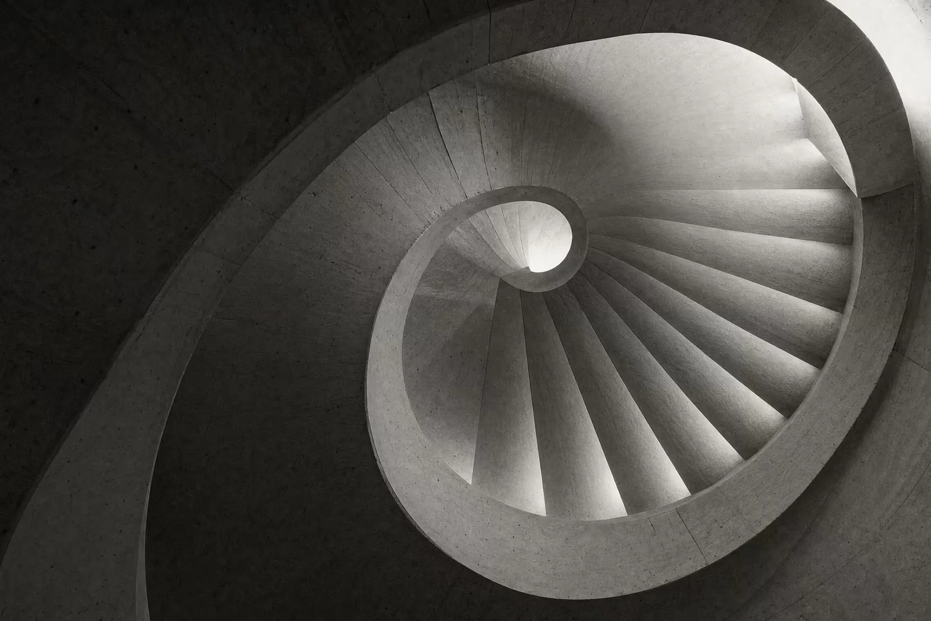 Cast-concrete spiral stair lit from a central oculus, warm-tone monochrome.