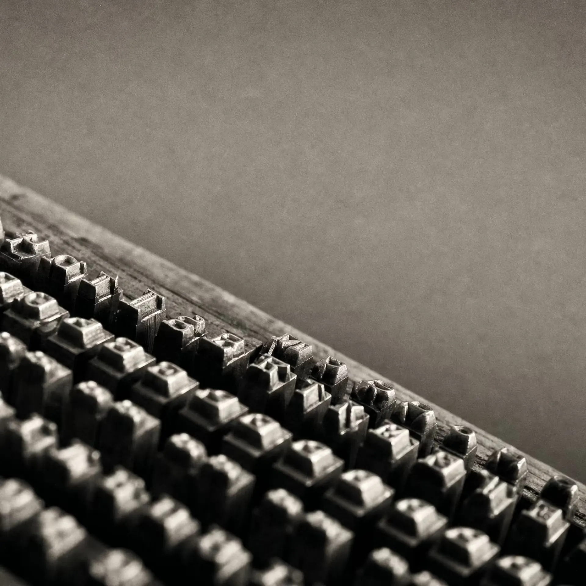 Rows of cast-metal letterpress type standing in a composing case, lit from one side in black and white, the character bodies receding in parallel ranks.