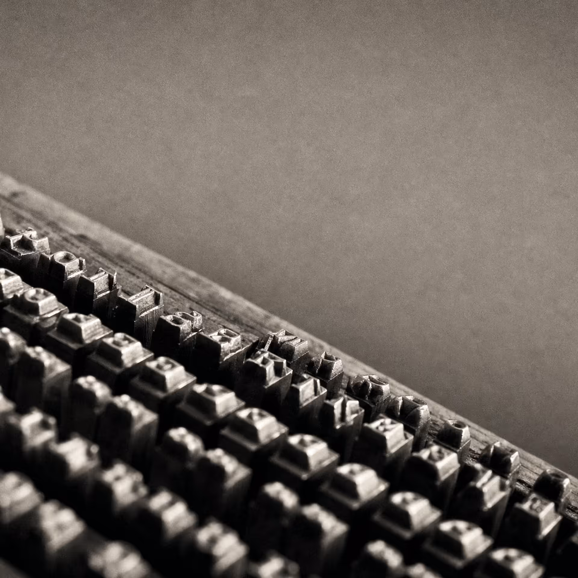 Rows of identical cast-metal letterpress type standing in a composing case in warm-tone monochrome, the character bodies receding in parallel ranks under grazing light.