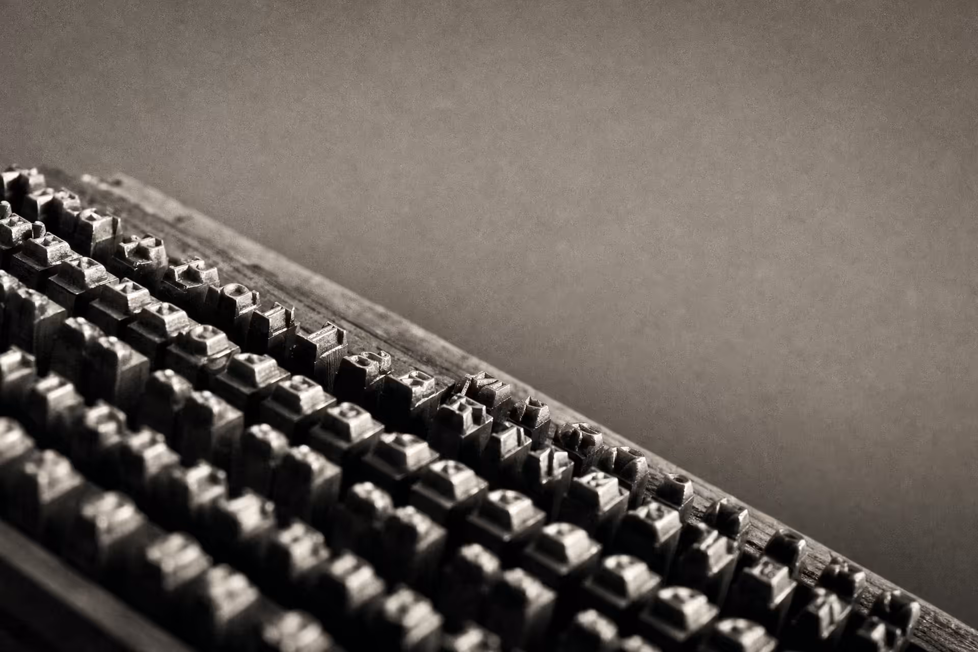 Rows of identical cast-metal letterpress type standing in a composing case in warm-tone monochrome, the character bodies receding in parallel ranks under grazing light.