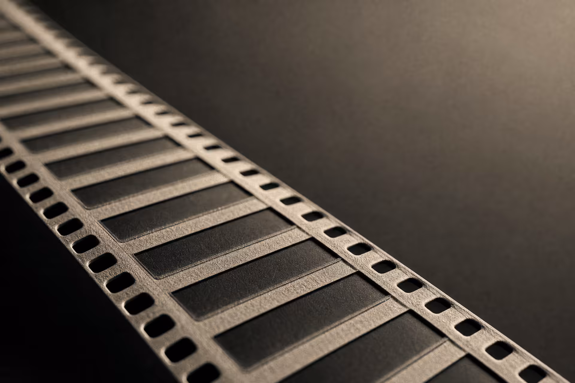 A strip of motion-picture film in warm-tone monochrome, the identical frames and edge perforations receding in parallel ranks under grazing light.