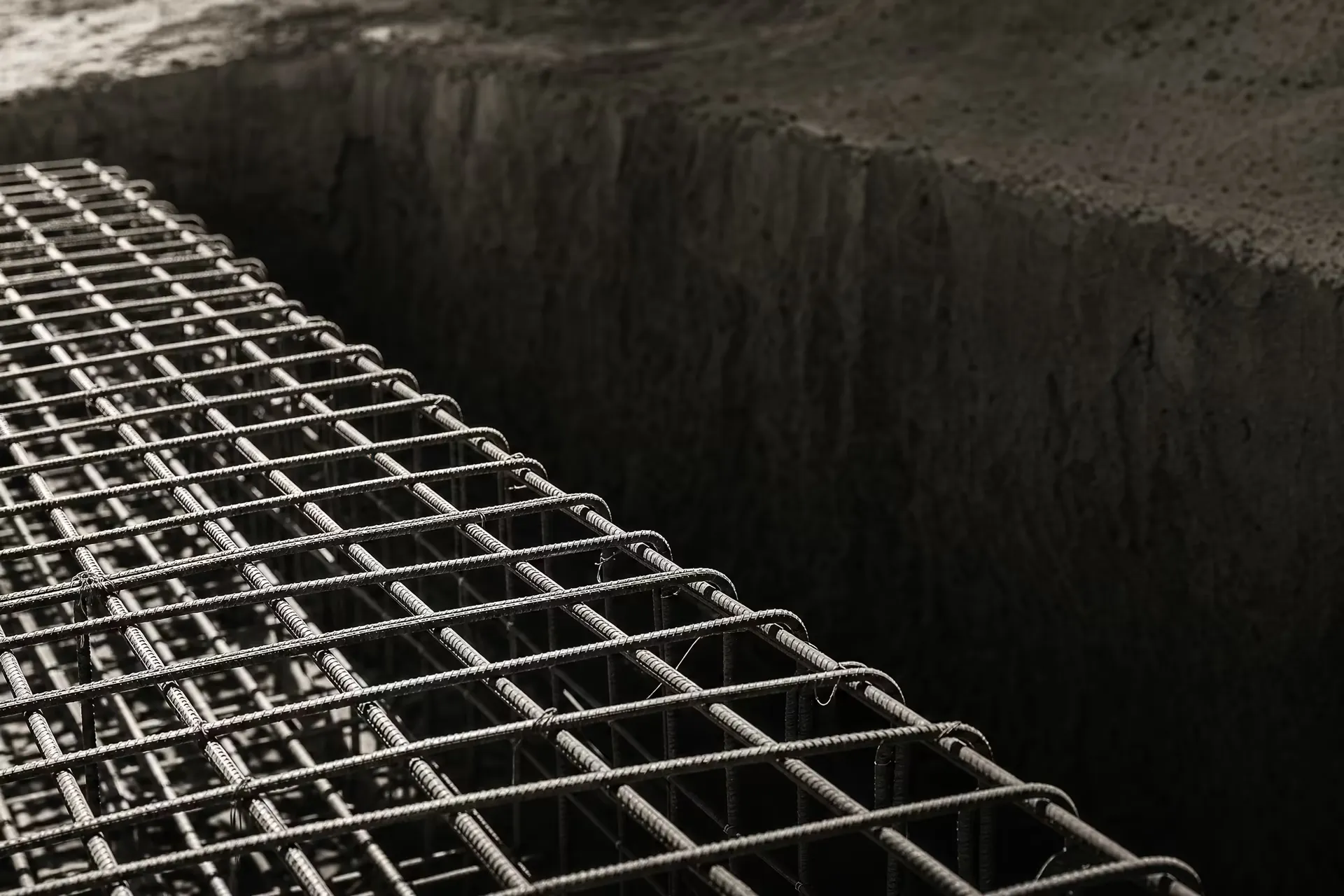 A dense lattice of steel reinforcing bar tied and waiting for the concrete pour, receding in parallel ranks under flat overhead light, black and white.