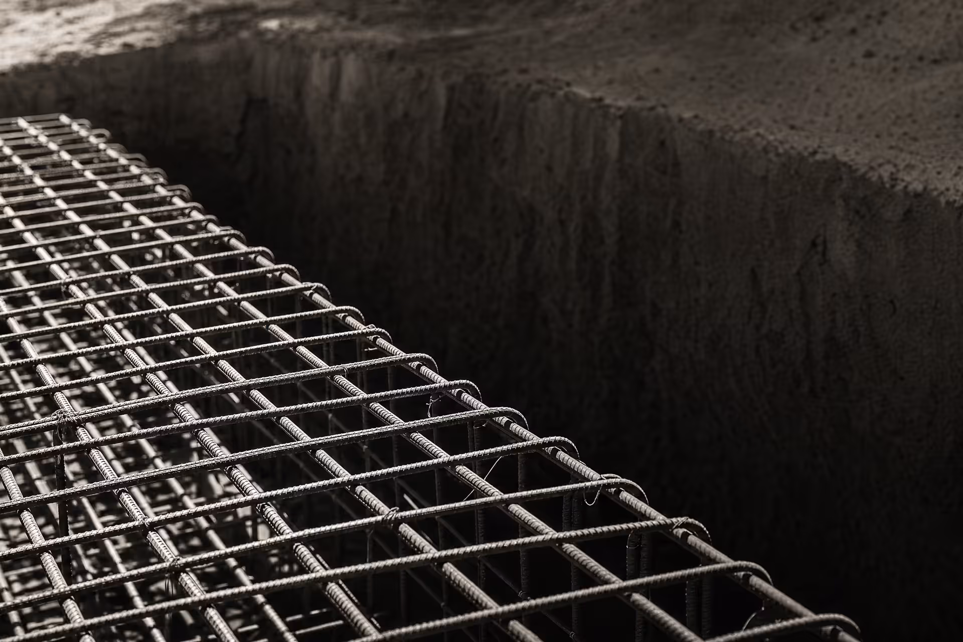 A dense lattice of steel reinforcing bar tied and waiting for the concrete pour, receding in parallel ranks under flat overhead light, black and white.