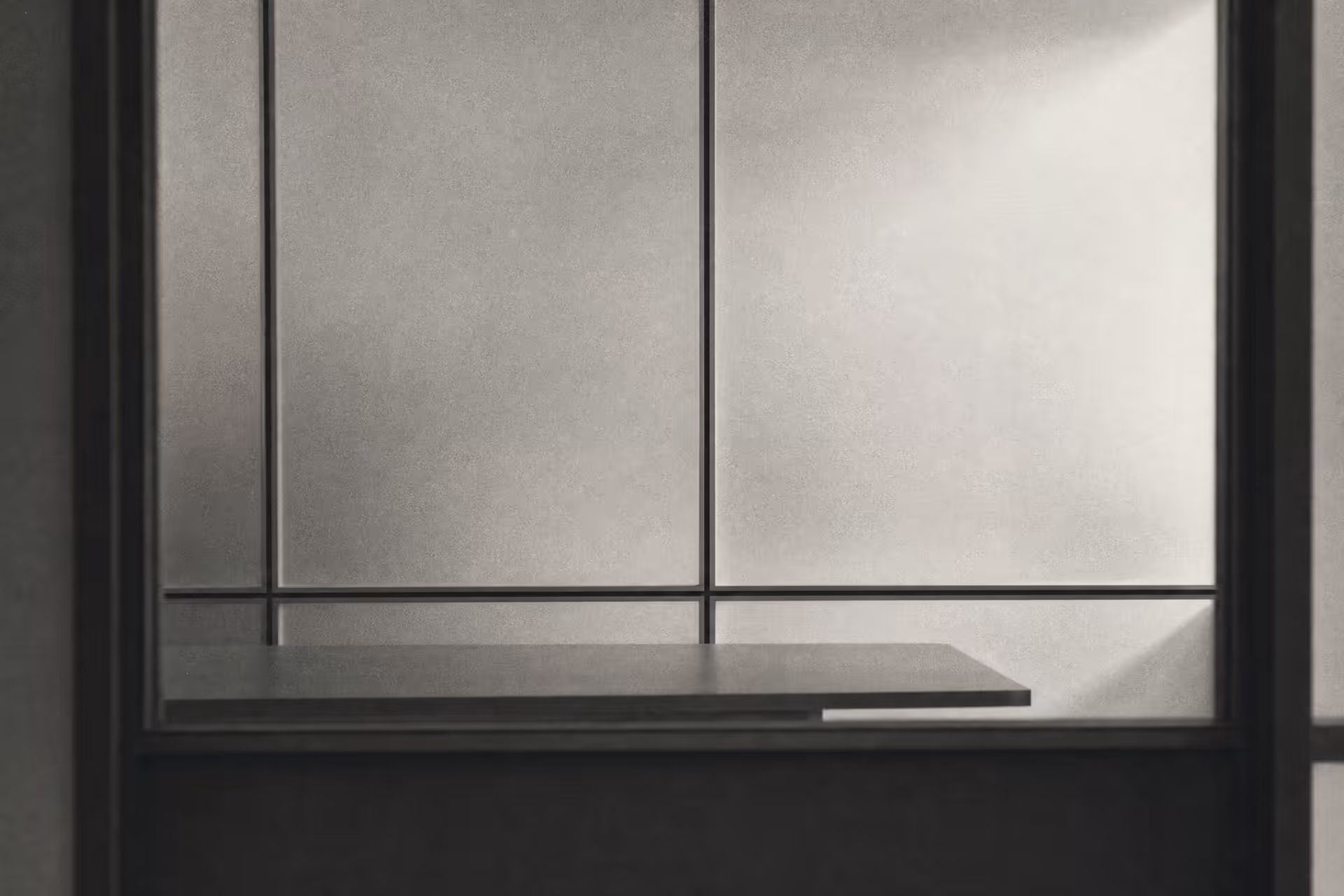 An empty meeting room seen through a frosted-glass partition, hairline aluminium frames dividing the panels into rectilinear sections, warm-tone monochrome.