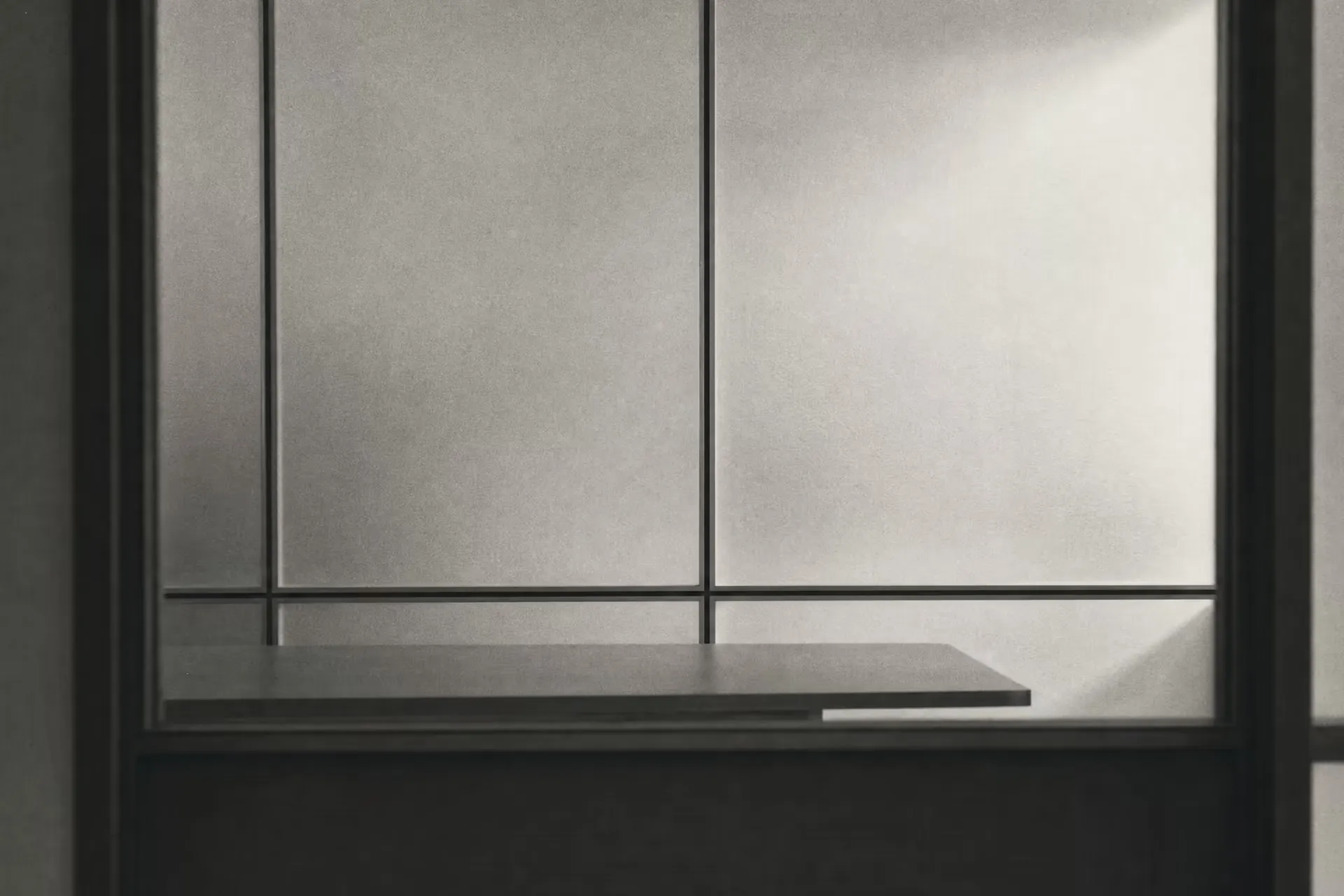 An empty meeting room seen through a frosted-glass partition, hairline aluminium frames dividing the panels into rectilinear sections, warm-tone monochrome.
