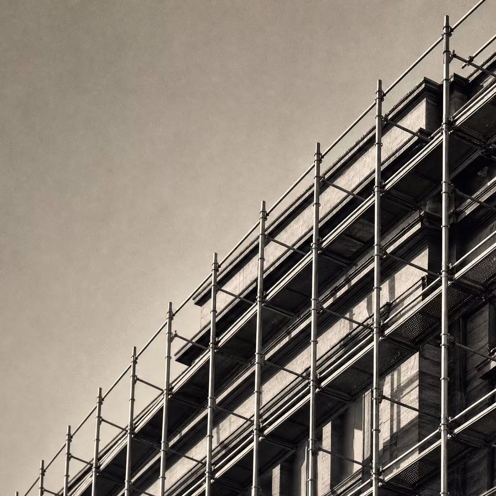 Steel scaffolding wrapping a stone building mid-renovation in warm-tone monochrome, the new tubular frame standing in front of the older facade as distinct planes.