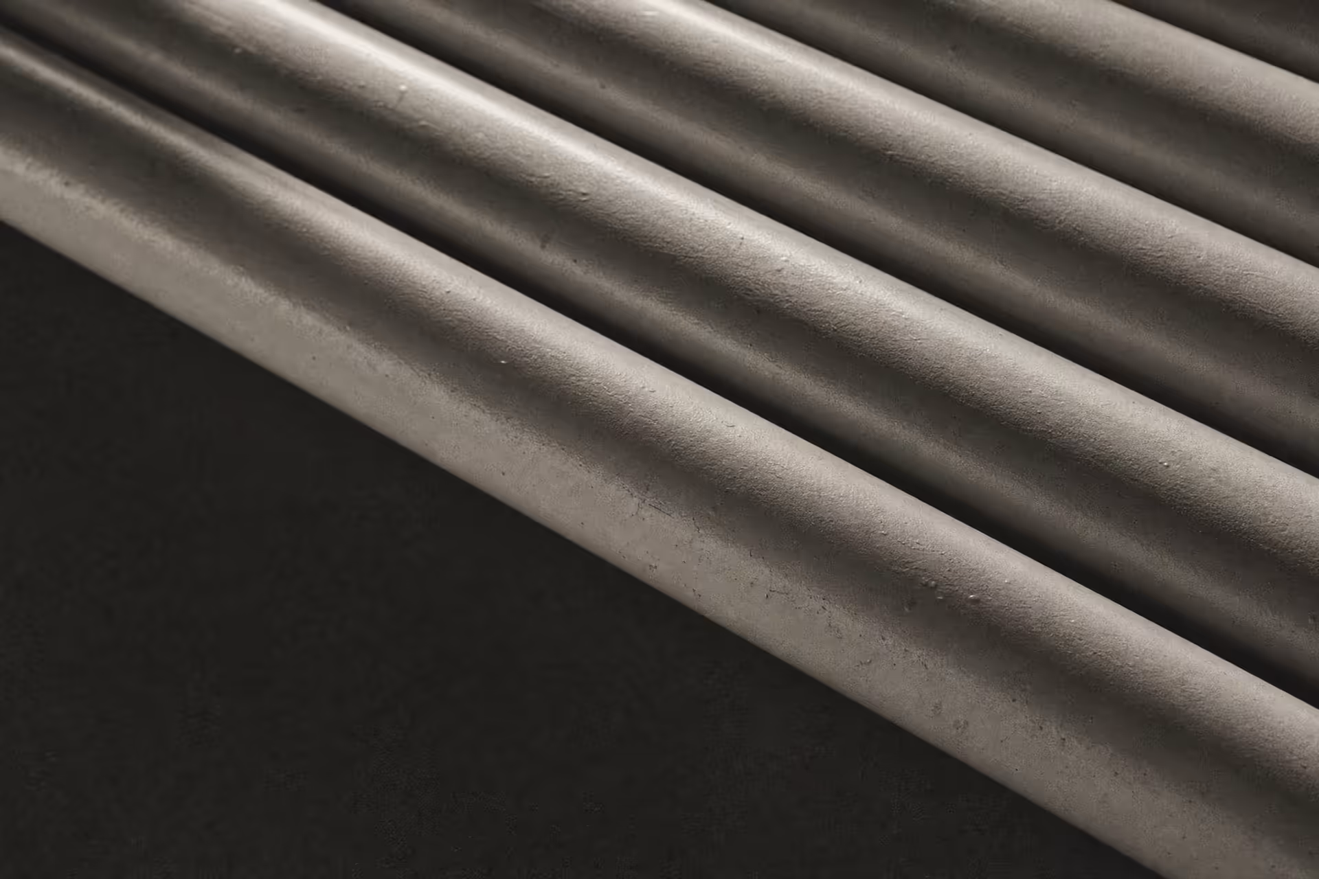 A dense run of polished steel pipework turning and branching through an industrial plant, parallel lines receding under flat overhead light, black and white.