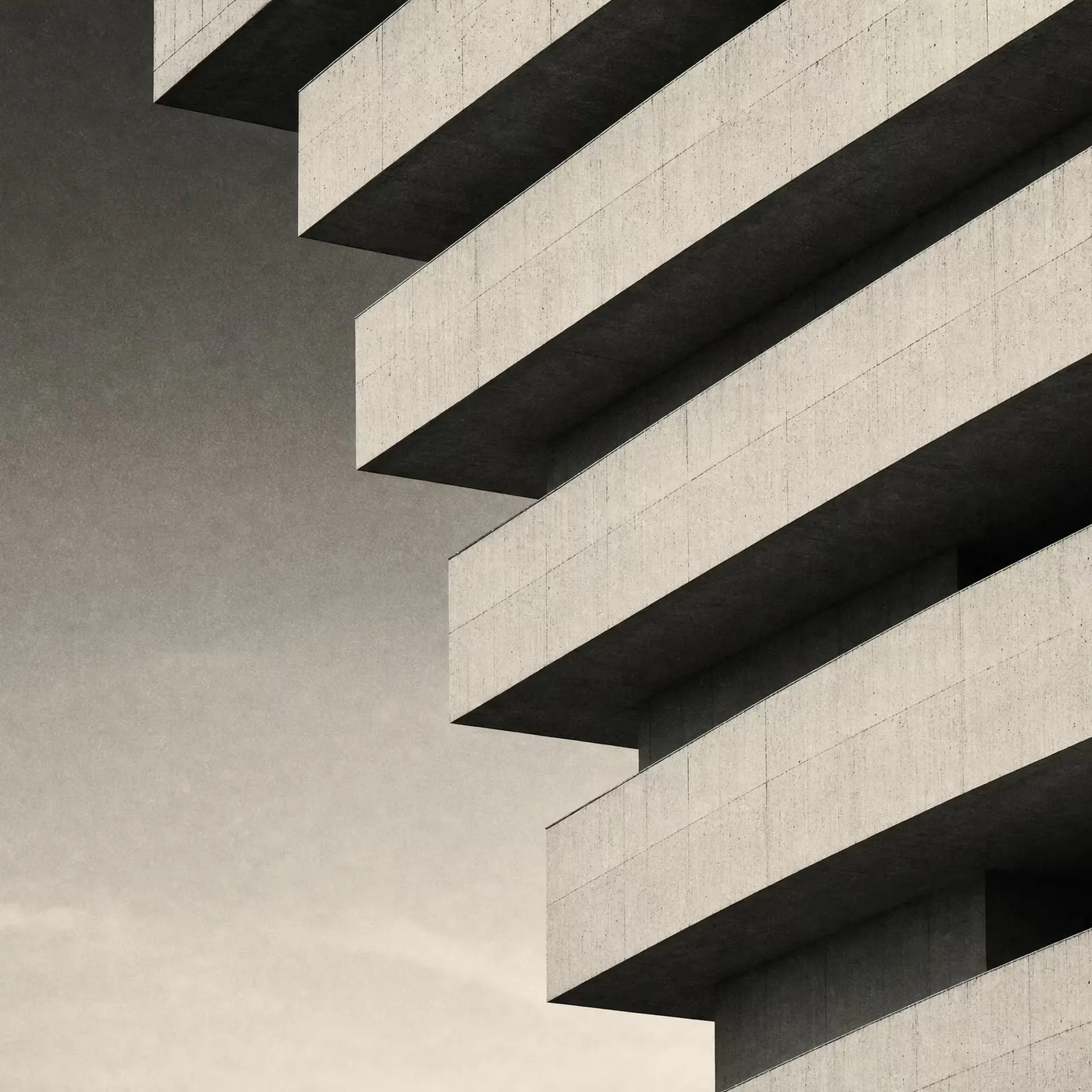 A layered precast-concrete facade in warm-tone monochrome, staggered horizontal bands stepping back floor by floor under raking daylight.