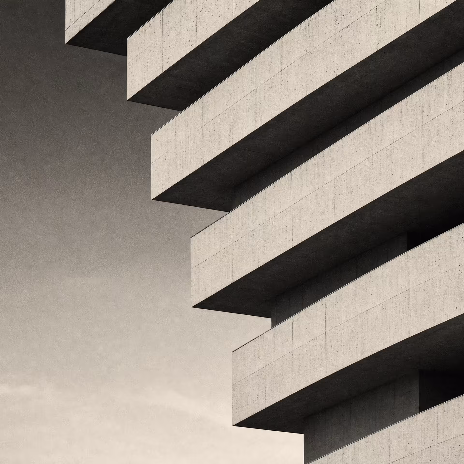 A layered precast-concrete facade in warm-tone monochrome, staggered horizontal bands stepping back floor by floor under raking daylight.