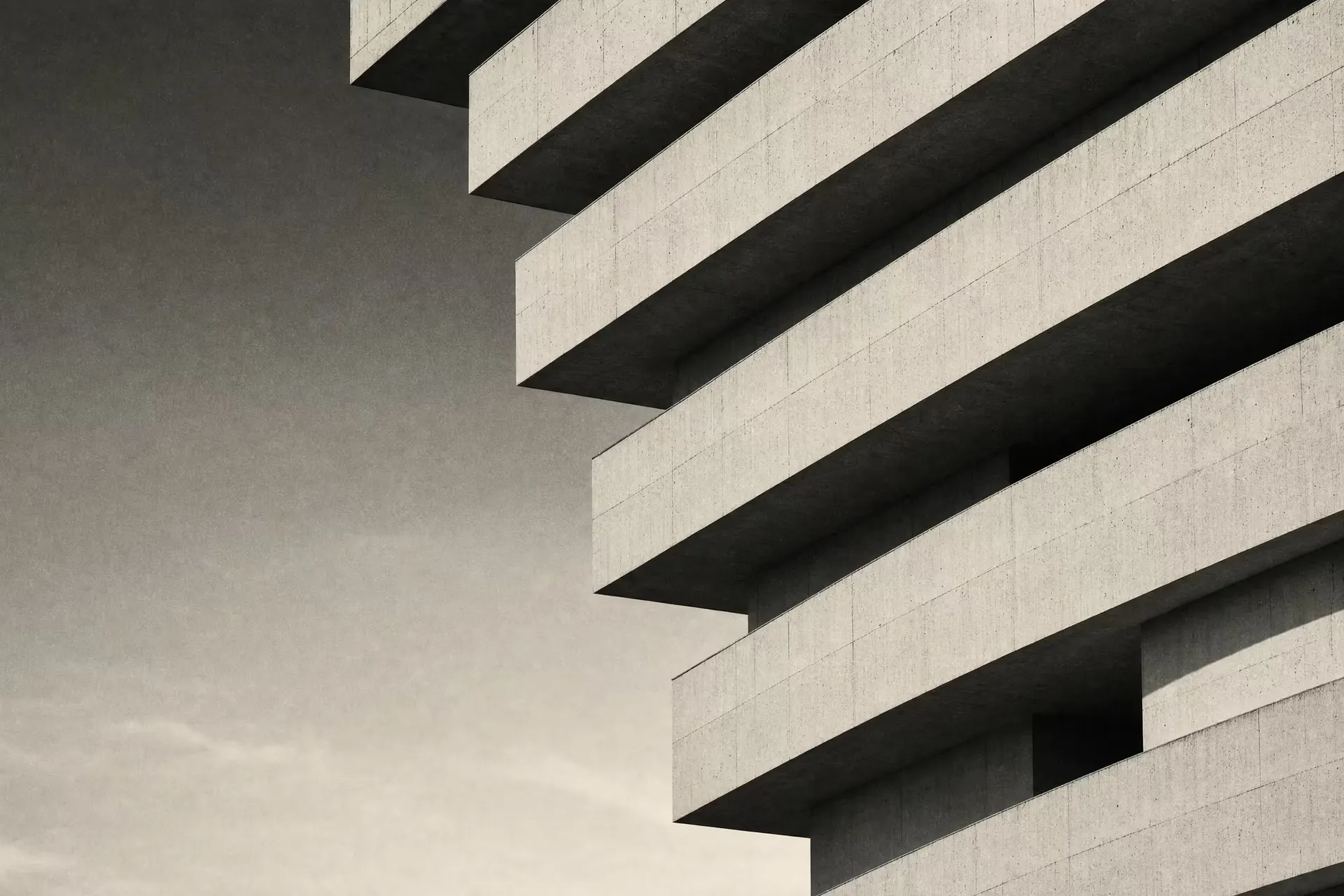 A layered precast-concrete facade in warm-tone monochrome, staggered horizontal bands stepping back floor by floor under raking daylight.
