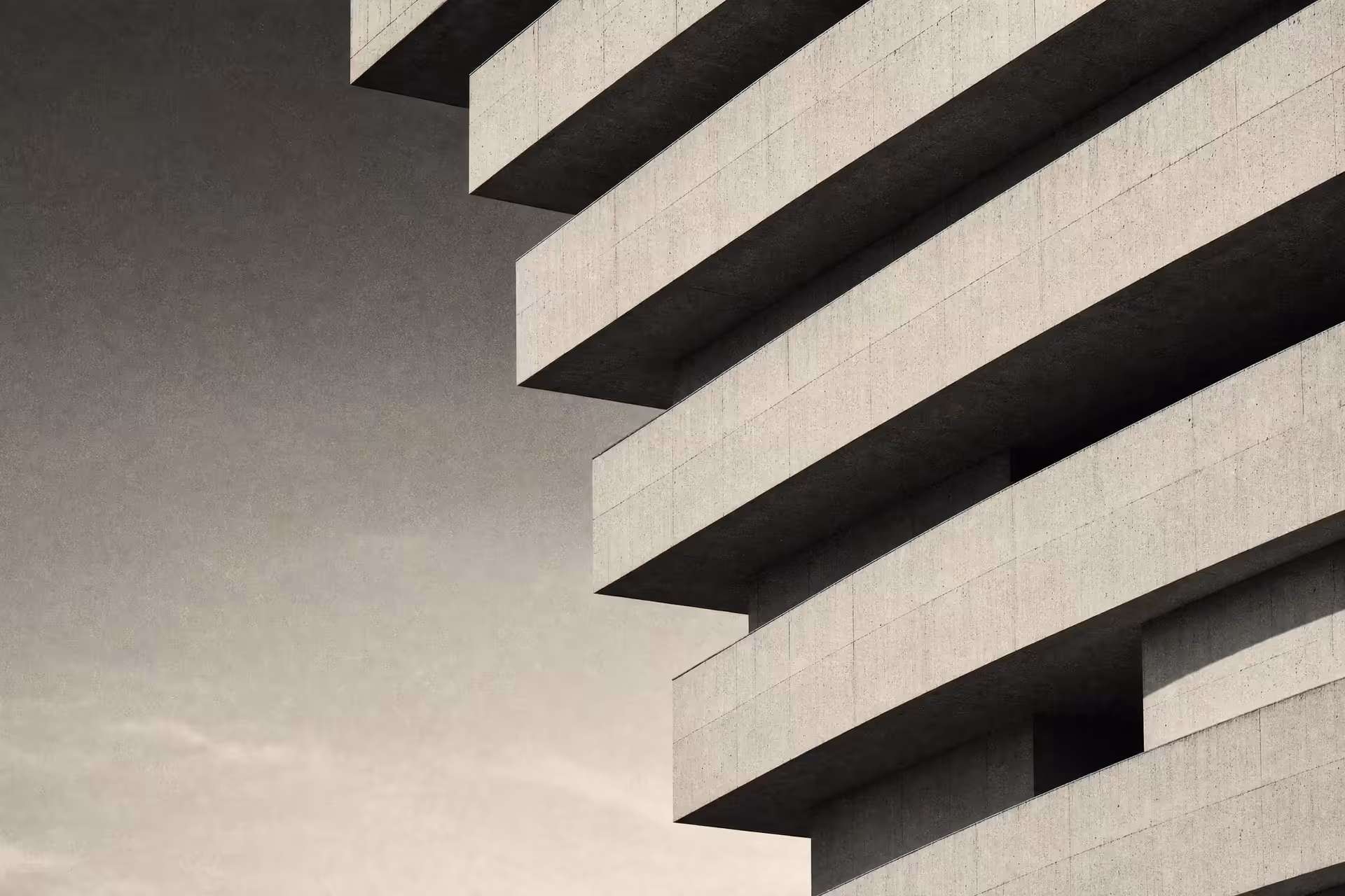 A layered precast-concrete facade in warm-tone monochrome, staggered horizontal bands stepping back floor by floor under raking daylight.