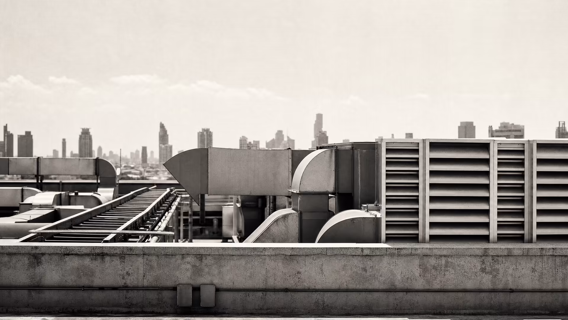 Bangkok office-building rooftop in warm-tone monochrome: HVAC ducts and metal louvres in sharp geometry, hazy city silhouettes reduced to tonal bands above.