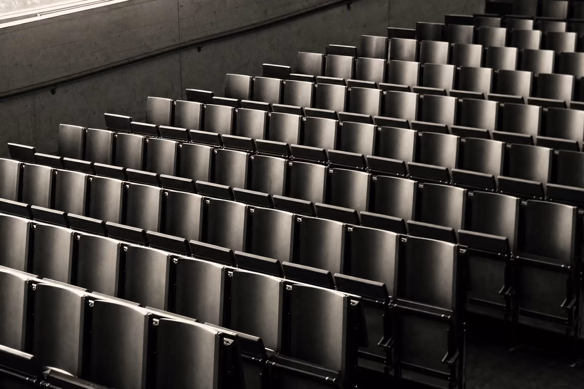 An empty tiered lecture hall, repeating rows of seats receding across the frame, warm-tone monochrome.