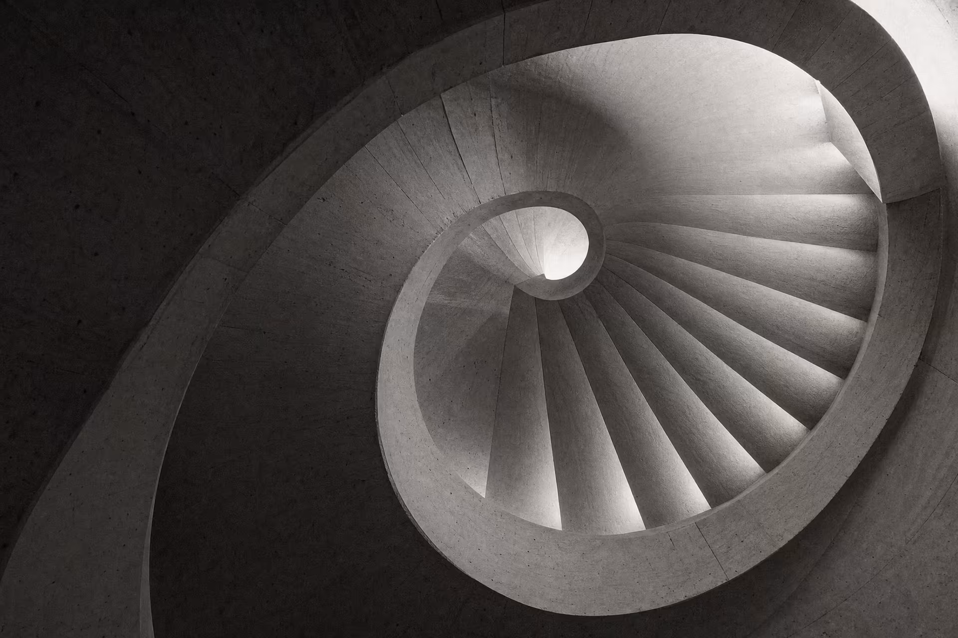 Cast-concrete spiral stair lit from a central oculus, warm-tone monochrome.